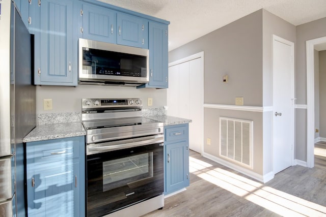 kitchen featuring stainless steel appliances, a textured ceiling, and light hardwood / wood-style floors