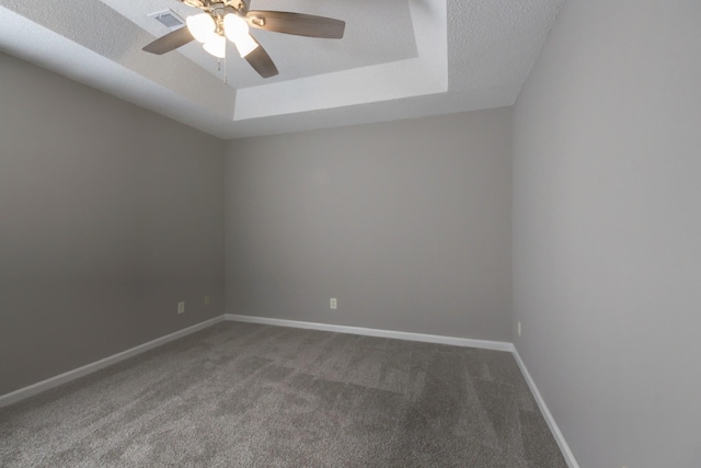 empty room with a textured ceiling, carpet floors, ceiling fan, and a tray ceiling