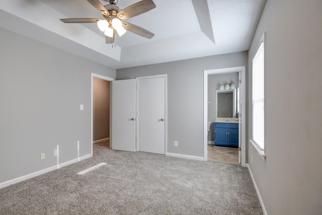 unfurnished bedroom featuring light carpet, connected bathroom, a raised ceiling, and ceiling fan