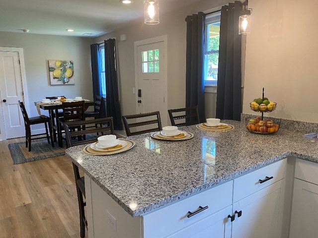 kitchen featuring pendant lighting, white cabinets, light stone countertops, light wood-type flooring, and a breakfast bar area