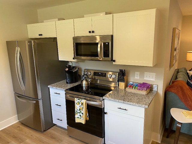 kitchen with light stone countertops, white cabinetry, light hardwood / wood-style flooring, and stainless steel appliances