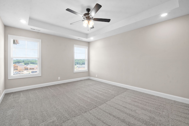 empty room featuring carpet flooring, a tray ceiling, and ceiling fan