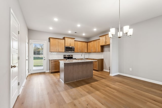 kitchen featuring sink, light wood-type flooring, an island with sink, appliances with stainless steel finishes, and light stone counters