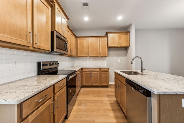 kitchen featuring light stone countertops, stainless steel appliances, sink, a center island with sink, and light hardwood / wood-style flooring