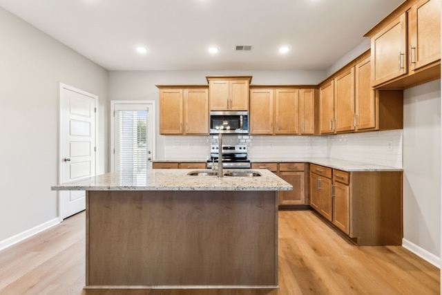 kitchen with sink, light hardwood / wood-style flooring, an island with sink, light stone counters, and stainless steel appliances