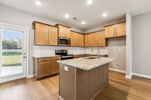 kitchen featuring sink, light hardwood / wood-style flooring, light stone countertops, an island with sink, and appliances with stainless steel finishes