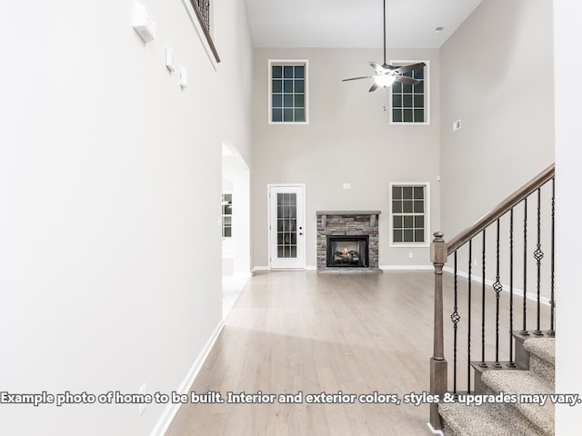 unfurnished living room with a high ceiling, a stone fireplace, ceiling fan, and wood-type flooring