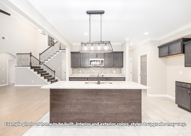 kitchen with light stone countertops, sink, crown molding, and an island with sink