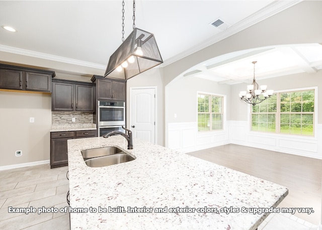 kitchen featuring dark brown cabinets, light stone countertops, sink, and hanging light fixtures