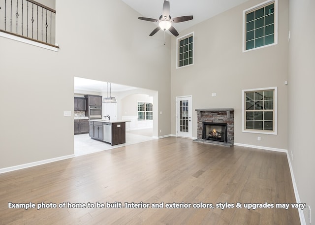 unfurnished living room featuring a fireplace, ceiling fan, light hardwood / wood-style flooring, and a towering ceiling