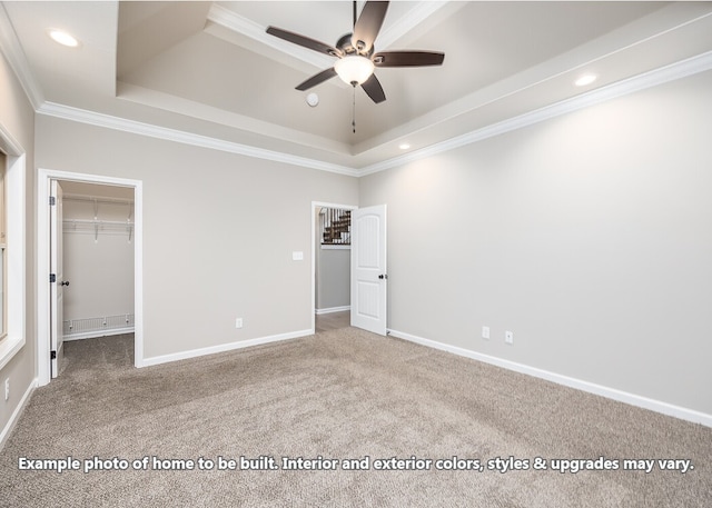 unfurnished bedroom with a tray ceiling, ceiling fan, crown molding, and a spacious closet