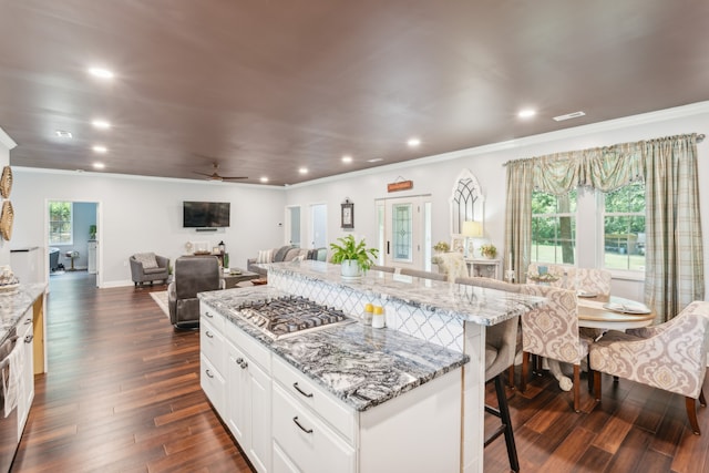 kitchen with light stone counters, a spacious island, a kitchen bar, white cabinetry, and ceiling fan