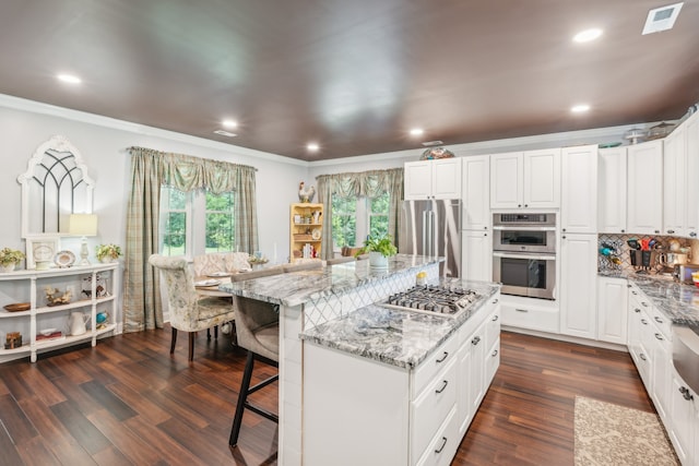 kitchen with appliances with stainless steel finishes, light stone countertops, a kitchen bar, a kitchen island, and white cabinets