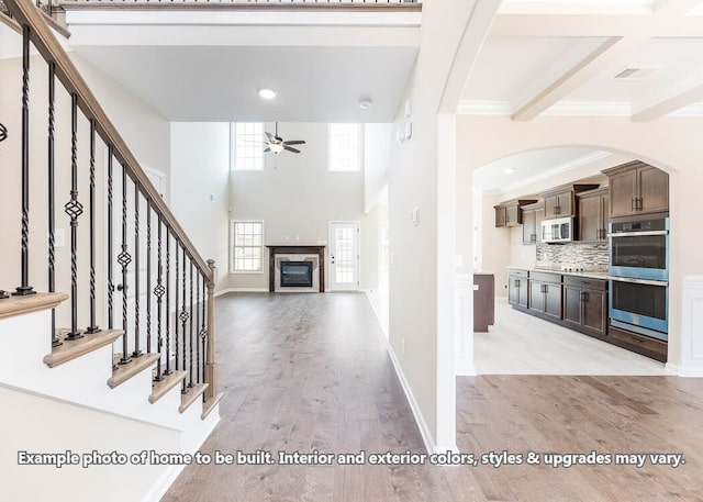 entryway with ceiling fan, stairs, ornamental molding, light wood-type flooring, and a glass covered fireplace