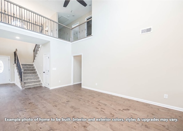 unfurnished living room featuring wood finished floors, visible vents, baseboards, a ceiling fan, and stairway