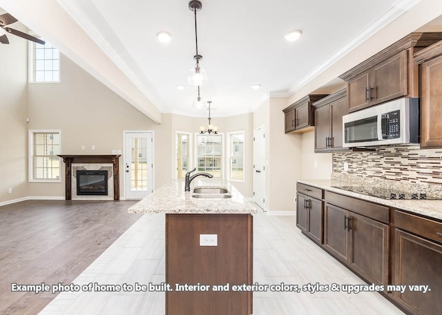 kitchen with black electric stovetop, stainless steel microwave, backsplash, a sink, and plenty of natural light