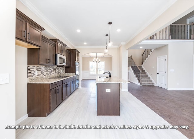 kitchen featuring a center island with sink, appliances with stainless steel finishes, ornamental molding, dark brown cabinets, and a sink