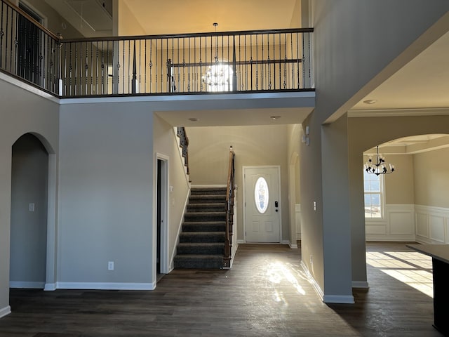 entrance foyer with arched walkways, a high ceiling, wood finished floors, and an inviting chandelier