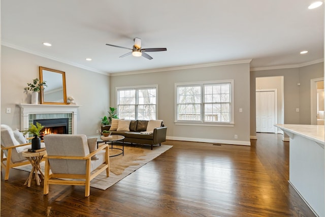 living room featuring a tile fireplace, ornamental molding, ceiling fan, and dark wood-type flooring