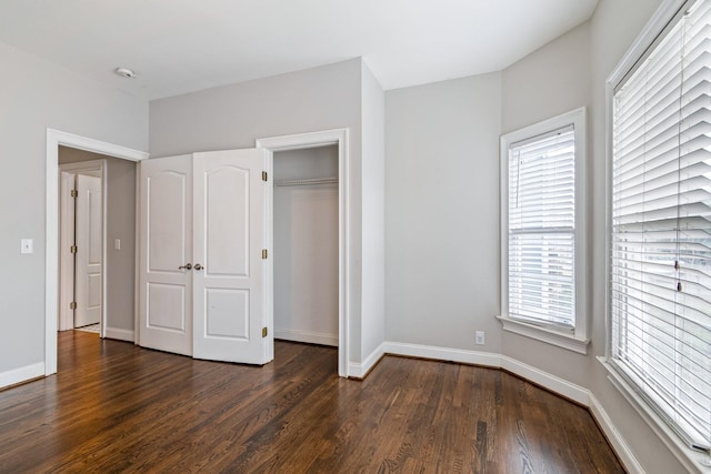 unfurnished bedroom with multiple windows, a closet, and dark hardwood / wood-style floors