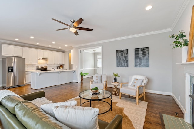 living room with a tile fireplace, hardwood / wood-style flooring, ceiling fan, and crown molding