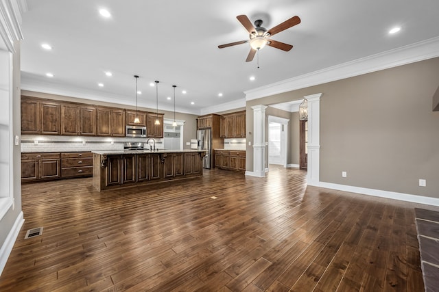 kitchen featuring dark hardwood / wood-style flooring, decorative columns, pendant lighting, a center island with sink, and appliances with stainless steel finishes