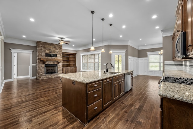 kitchen with a center island with sink, hanging light fixtures, a fireplace, appliances with stainless steel finishes, and dark hardwood / wood-style flooring