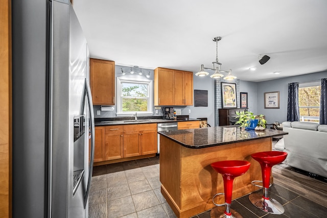 kitchen with sink, hanging light fixtures, stainless steel appliances, a breakfast bar, and a kitchen island