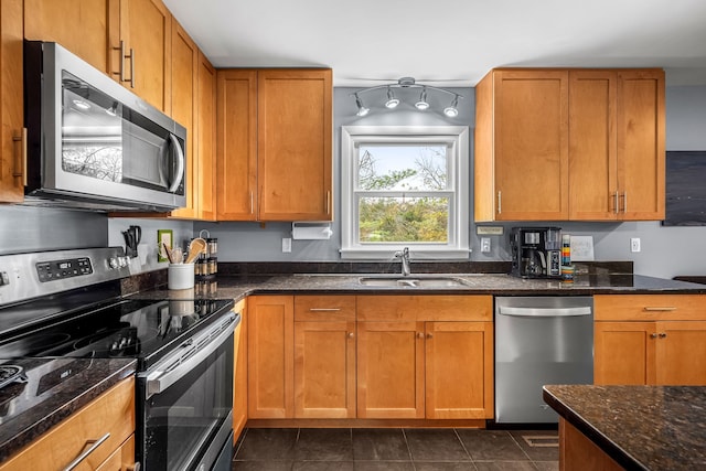 kitchen with stainless steel appliances, dark tile patterned flooring, dark stone countertops, and sink