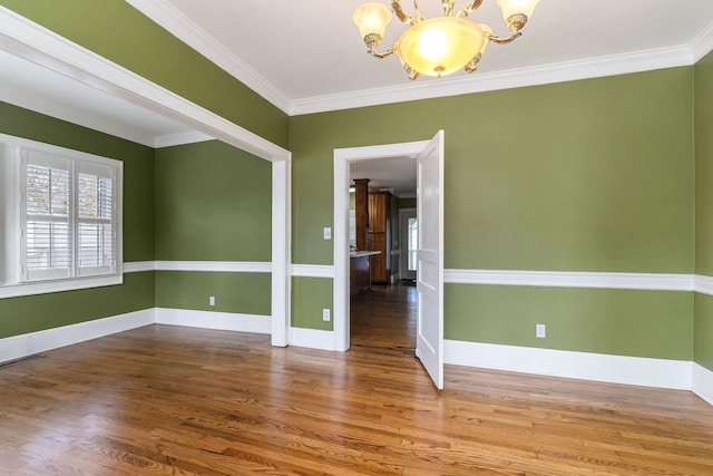 spare room featuring hardwood / wood-style floors, crown molding, and an inviting chandelier