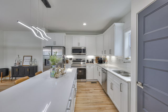 kitchen featuring backsplash, stainless steel appliances, decorative light fixtures, light hardwood / wood-style flooring, and white cabinetry