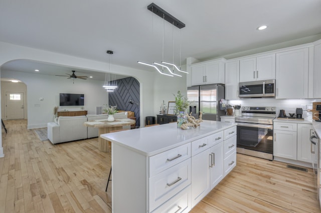 kitchen featuring appliances with stainless steel finishes, decorative light fixtures, white cabinetry, and light hardwood / wood-style flooring