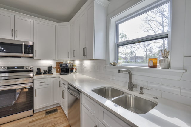 kitchen featuring appliances with stainless steel finishes, tasteful backsplash, sink, light hardwood / wood-style flooring, and white cabinetry