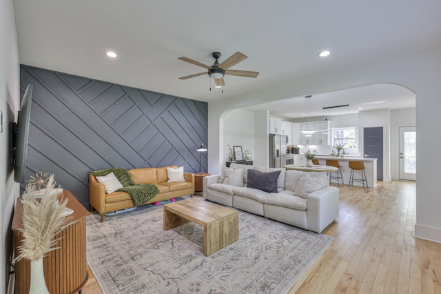 living room with ceiling fan, wooden walls, and light hardwood / wood-style flooring