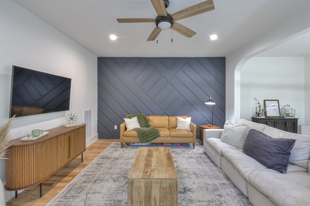 living room with light hardwood / wood-style flooring, ceiling fan, and wood walls