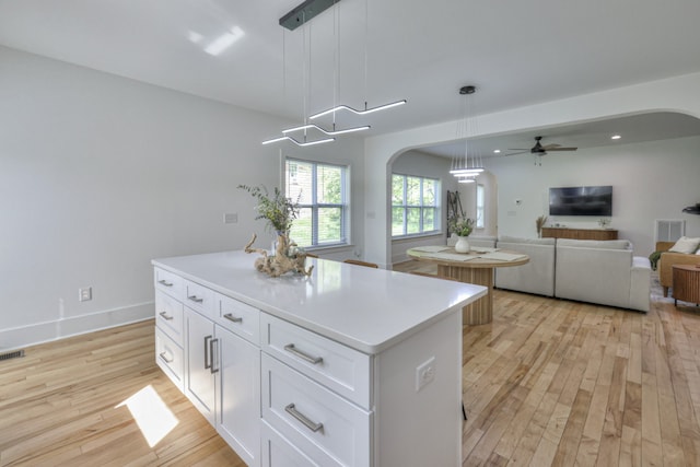 kitchen with light hardwood / wood-style flooring, ceiling fan, decorative light fixtures, a kitchen island, and white cabinetry