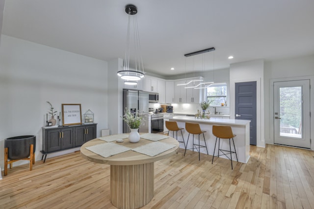 kitchen with white cabinetry, hanging light fixtures, light hardwood / wood-style flooring, a kitchen island, and appliances with stainless steel finishes