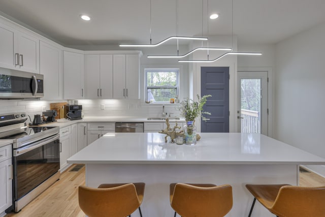 kitchen with white cabinetry, a kitchen island, stainless steel appliances, and light hardwood / wood-style floors