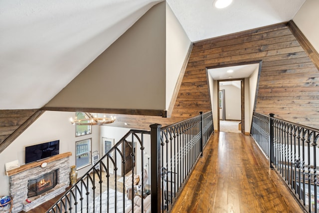 corridor with hardwood / wood-style flooring, a notable chandelier, wood walls, and lofted ceiling