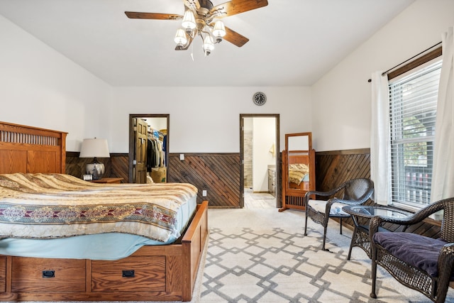 bedroom with wood walls, a walk in closet, ceiling fan, light colored carpet, and a closet