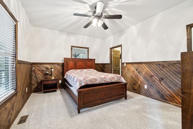 bedroom with ceiling fan, light carpet, and wooden walls