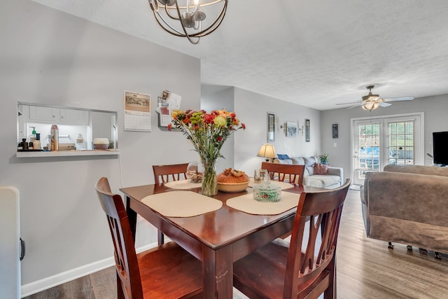 dining space with ceiling fan with notable chandelier, wood-type flooring, and a textured ceiling