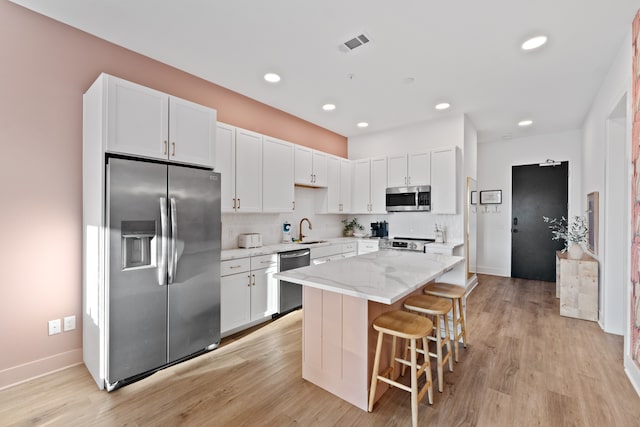 kitchen featuring sink, a center island, light stone counters, white cabinets, and appliances with stainless steel finishes