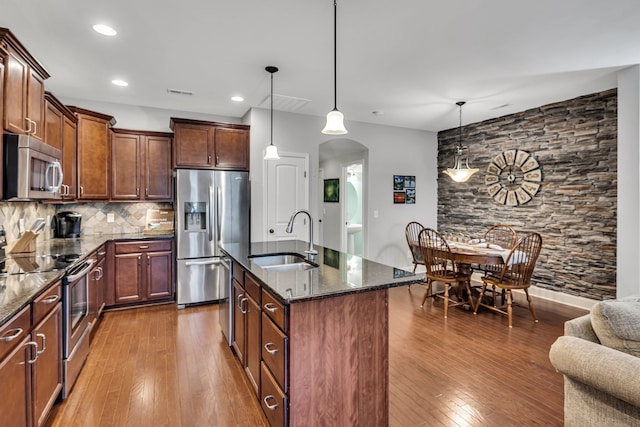 kitchen featuring sink, hanging light fixtures, wood-type flooring, a kitchen island with sink, and appliances with stainless steel finishes