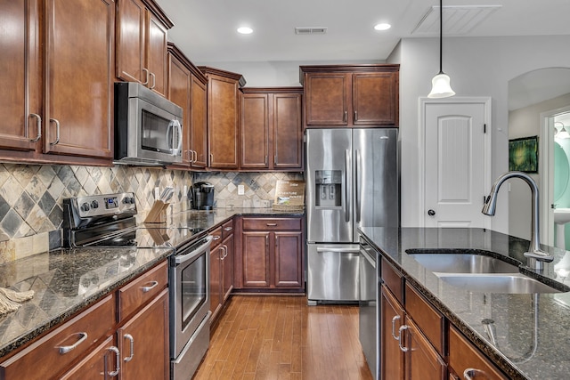 kitchen featuring sink, stainless steel appliances, dark stone countertops, pendant lighting, and light wood-type flooring