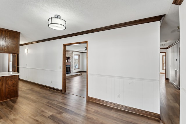 spare room with dark wood-type flooring, a textured ceiling, a brick fireplace, and ornamental molding