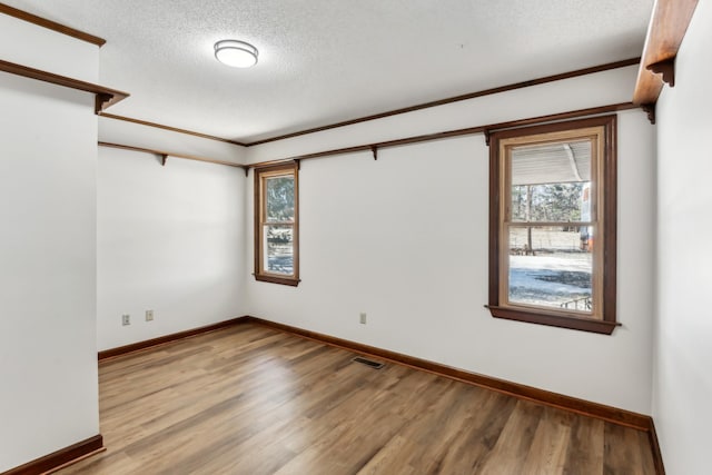 empty room featuring hardwood / wood-style flooring, crown molding, plenty of natural light, and a textured ceiling