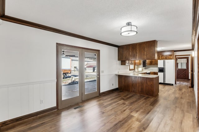 kitchen with a textured ceiling, white refrigerator with ice dispenser, dark hardwood / wood-style floors, kitchen peninsula, and crown molding