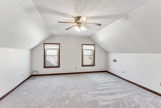 bonus room with light colored carpet, a textured ceiling, vaulted ceiling, and ceiling fan