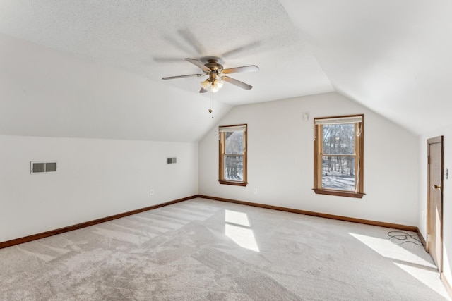 bonus room featuring light colored carpet, a textured ceiling, vaulted ceiling, and ceiling fan